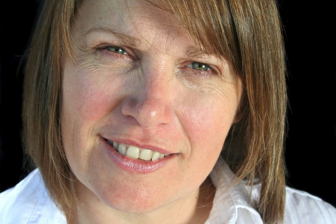 Woman smiling gently, her cheeks slightly flushed, reflecting the challenge of staying confident while speaking in public.