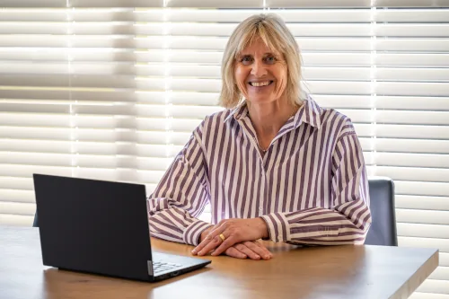 Catherine Syme seated at her desk with a laptop, smiling as she provides a one-on-one executive coaching session in public speaking.